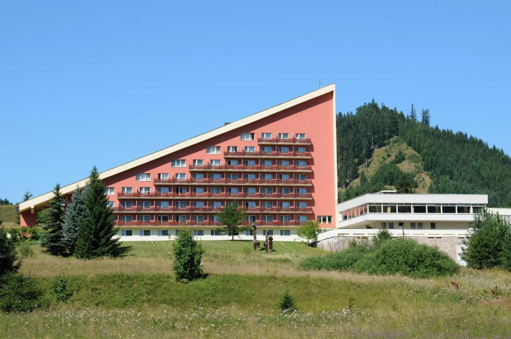 ein großes rotes Gebäude vor einem Berg in der Unterkunft Hotel SOREA MÁJ in Liptovský Ján