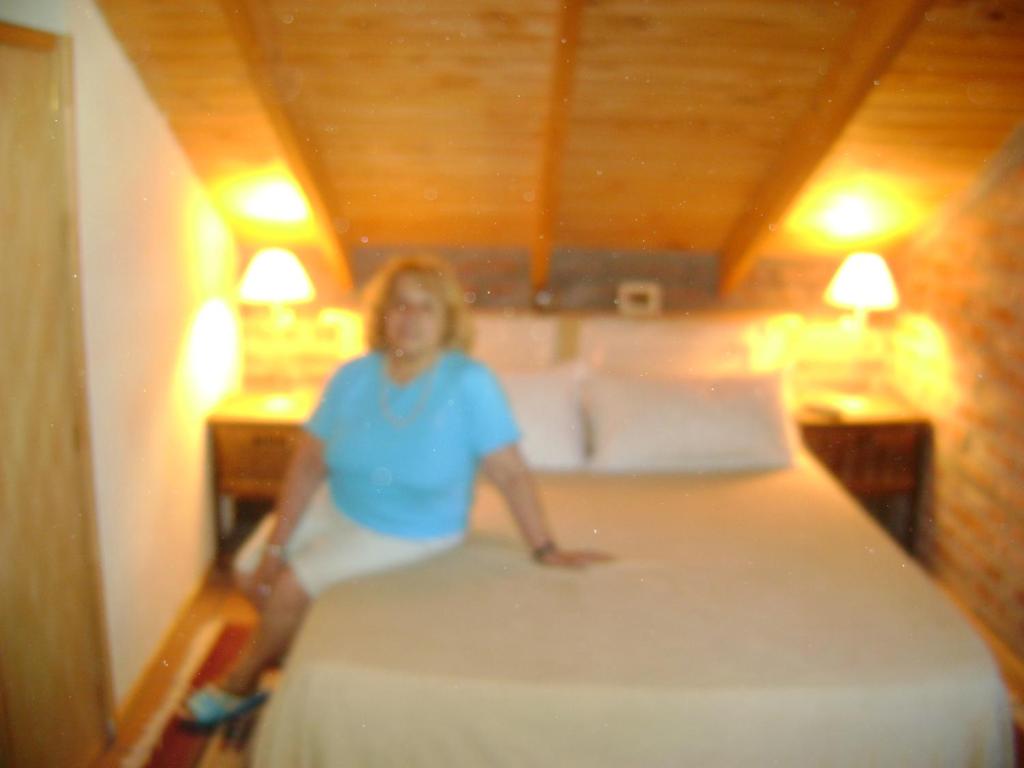 una mujer sentada en una cama en una habitación en Cabañas Ailen en Sierra de la Ventana