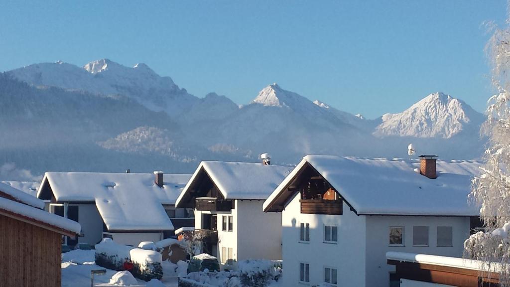 una casa con techos nevados con montañas al fondo en Ferienwohnung Johanna, en Schwangau