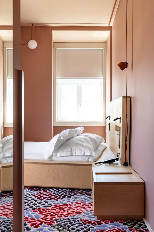 A narrow pink-toned bedroom with a window-facing bed, full-height mirror, patterned carpet, and built-in desk surface.