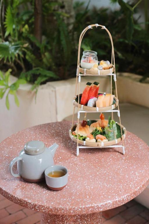 A tiered stand of fruit and pastries is served beside a pot of tea.
