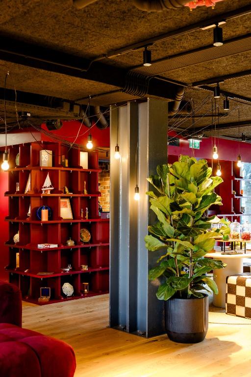 An industrial-style interior framed by a tall plant, red shelving, and exposed services.