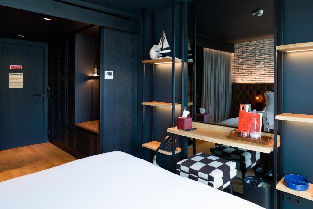 A dark-toned bedroom with a desk, checkered stool and exposed-brick bed alcove.