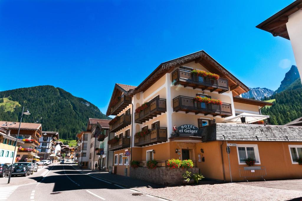 un bâtiment dans une rue avec des montagnes en arrière-plan dans l'établissement Hotel El Geiger, à Pozza di Fassa