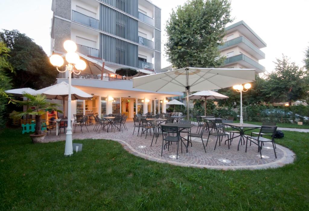 un patio al aire libre con mesas, sillas y sombrillas en Hotel Corona, en Riccione