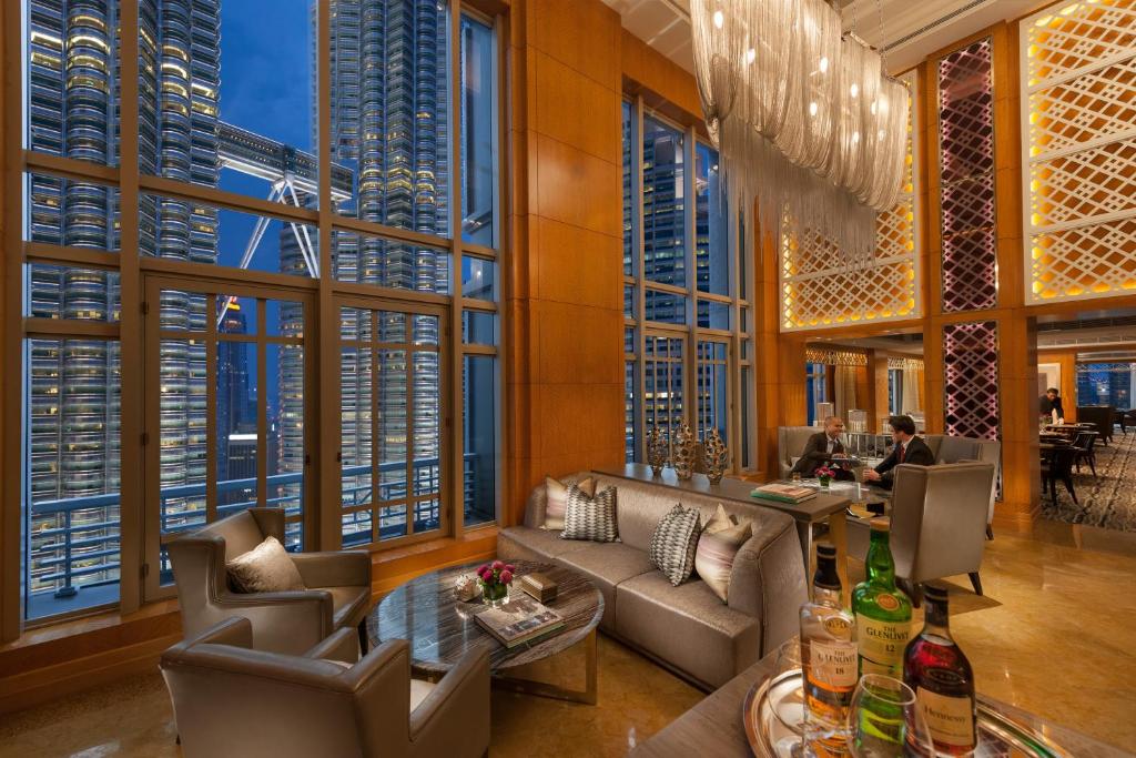 A high-windowed lounge overlooking illuminated city towers, with a bar area beyond.