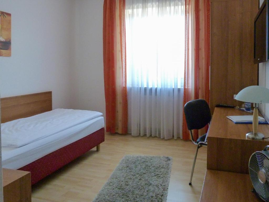 a bedroom with a bed and a desk and a window at City Hotel in Waldkraiburg