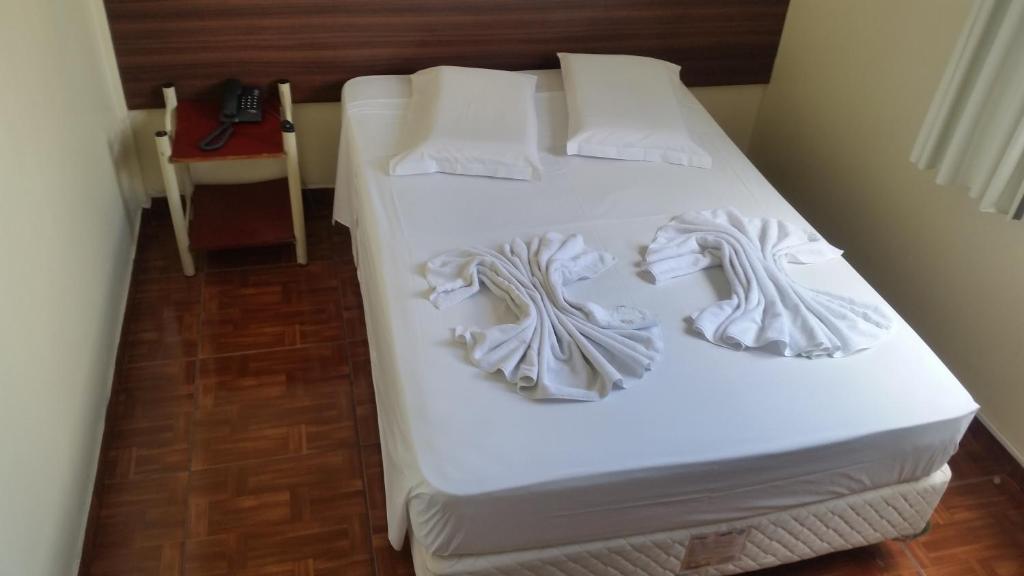 uma cama num quarto com lençóis brancos e almofadas em Hotel Piratini em Curitiba