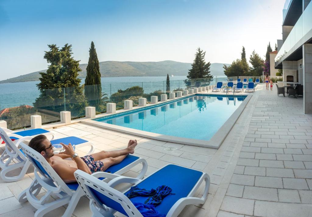 Ein Mann, der auf einem Stuhl neben einem Pool liegt. in der Unterkunft Trogir Residence Vila A in Seget Vranjica