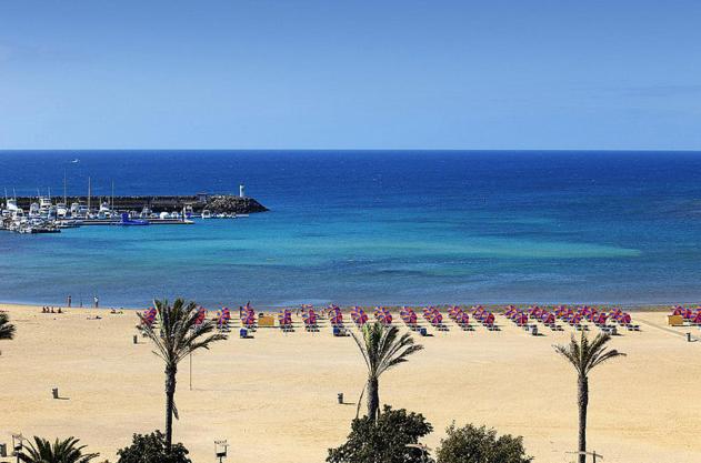 a beach with a bunch of umbrellas and palm trees at Puerta del sol in Caleta De Fuste