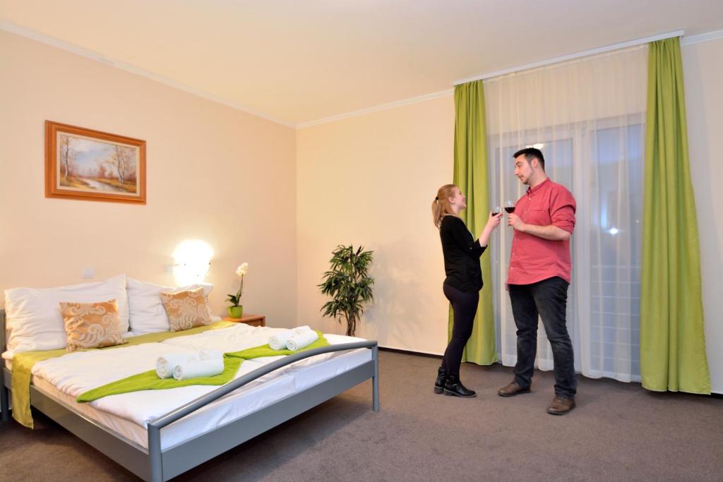a man and woman standing in a hotel room with a bed at Viktória Wellness Hotel in Nagyatád