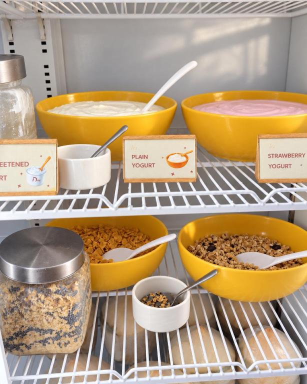 A refrigerated breakfast shelf with yogurt bowls, cereal, and serving spoons.