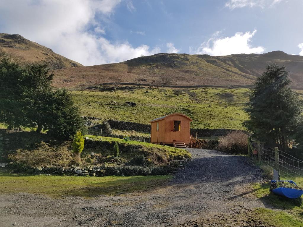 a barn on a hill with a dirt road at Stybeck Farm Shephards Hut in Thirlmere
