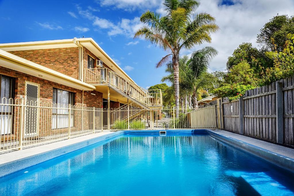 a swimming pool in front of a house with a fence at Allambi Holiday Apartments in Lakes Entrance
