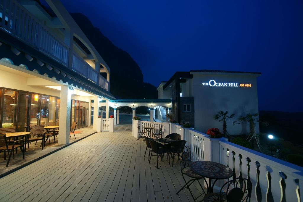 una terraza de madera con mesas y sillas por la noche en Jeju the Ocean Hill Pension en Seogwipo