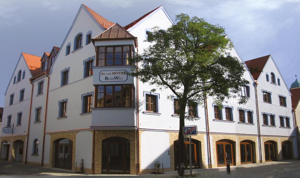 ein weißes Gebäude mit einem Baum davor in der Unterkunft Altstadthotel Bräuwirt in Weiden