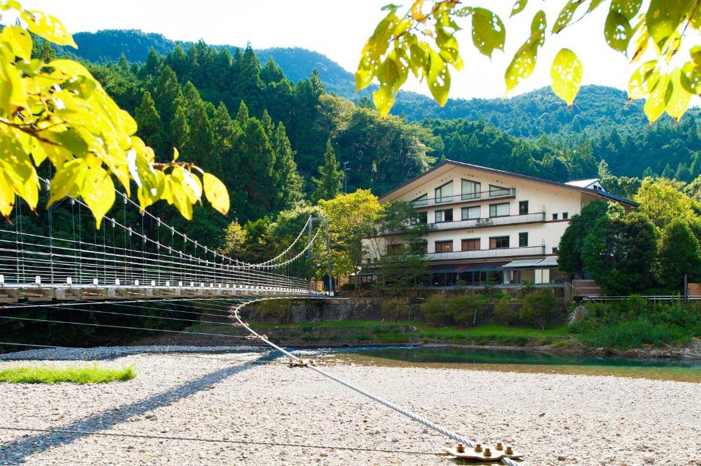 un puente colgante sobre un río junto a un edificio en Watarase Onsen Hotel Yamayuri en Hongu