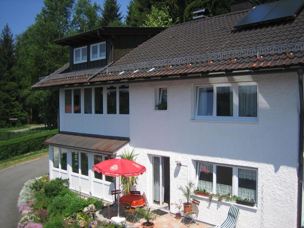 a white house with a red umbrella and a patio at Waldferienhof am Nationalpark in Spiegelau