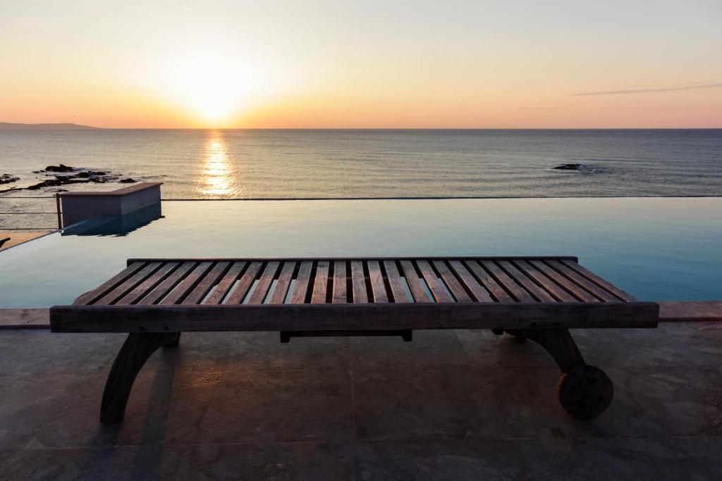 un banco de madera sentado junto al océano al atardecer en Beach Villa Pantheon, en Pomos