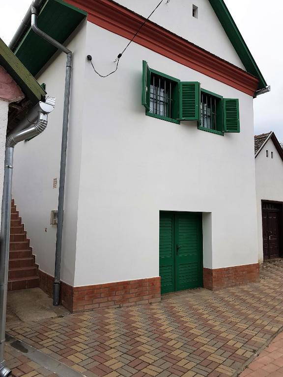 a white building with green doors and windows at Pincesor Apartman in Villánykövesd