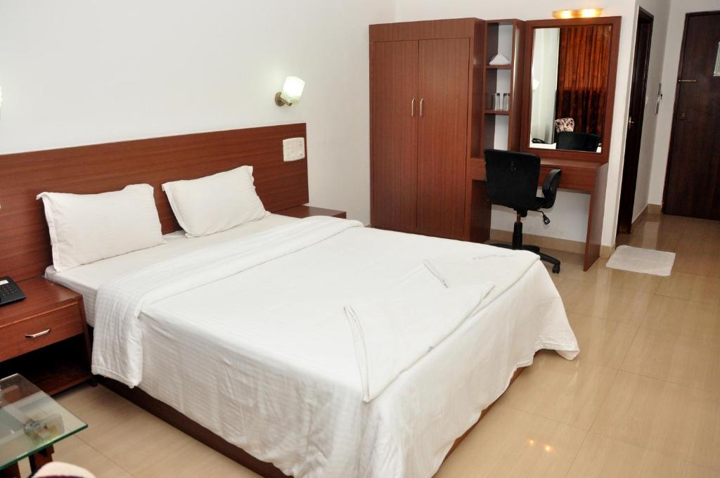 a bedroom with a large white bed and a desk at Emporium Hotel in Mangalore