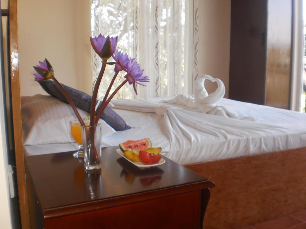 Una cama con una mesa con un bol de frutas y flores en Witherspoon Lodge en Kandy