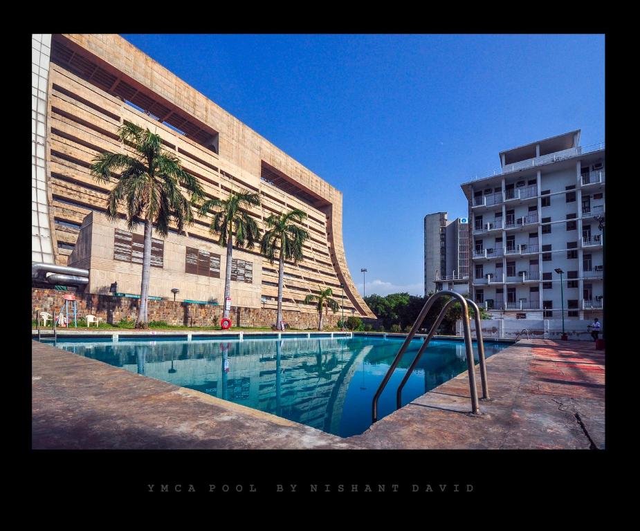 a swimming pool in front of a building with palm trees at New Delhi YMCA Tourist Hostel in New Delhi