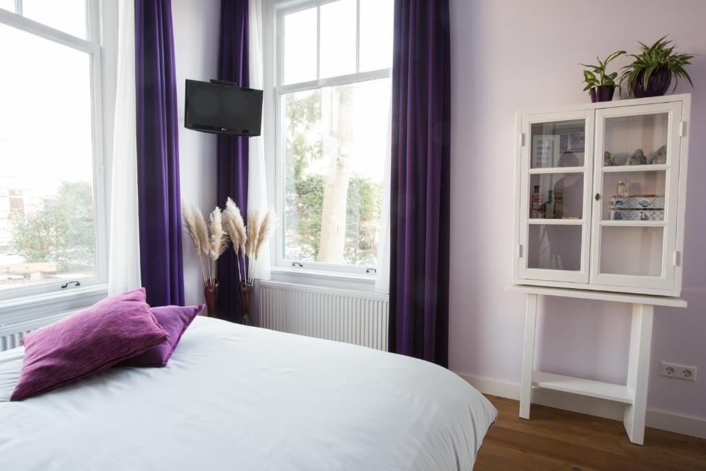 een slaapkamer met een wit bed en paarse gordijnen bij B&B Slapen bij de burgemeester in Sint Pancras