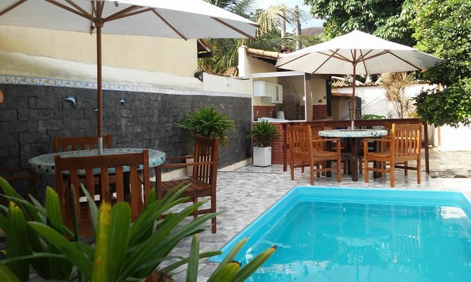 una piscina con sillas, mesas y sombrilla en Casa 6 Suites e Eventos en Itaipuaçu