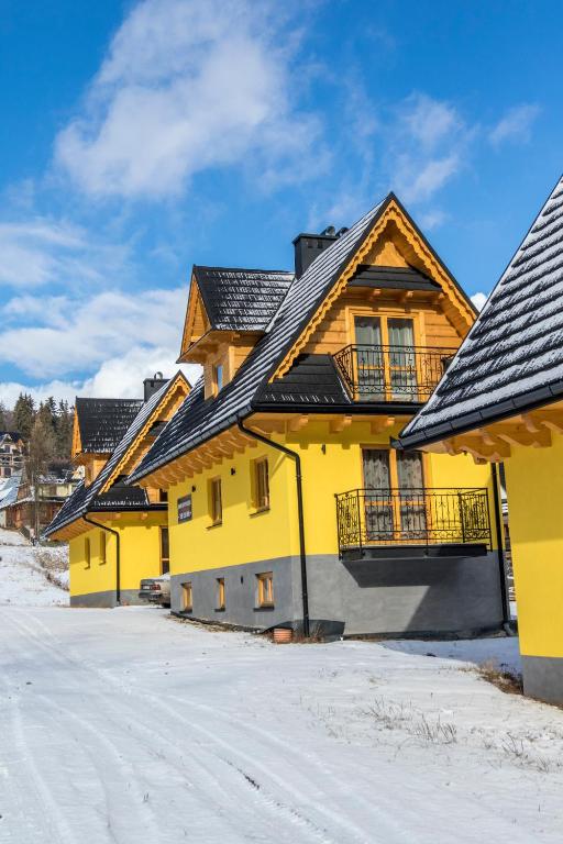 a yellow house with a black roof in the snow at Góralskie Zacisze Domki in Suche
