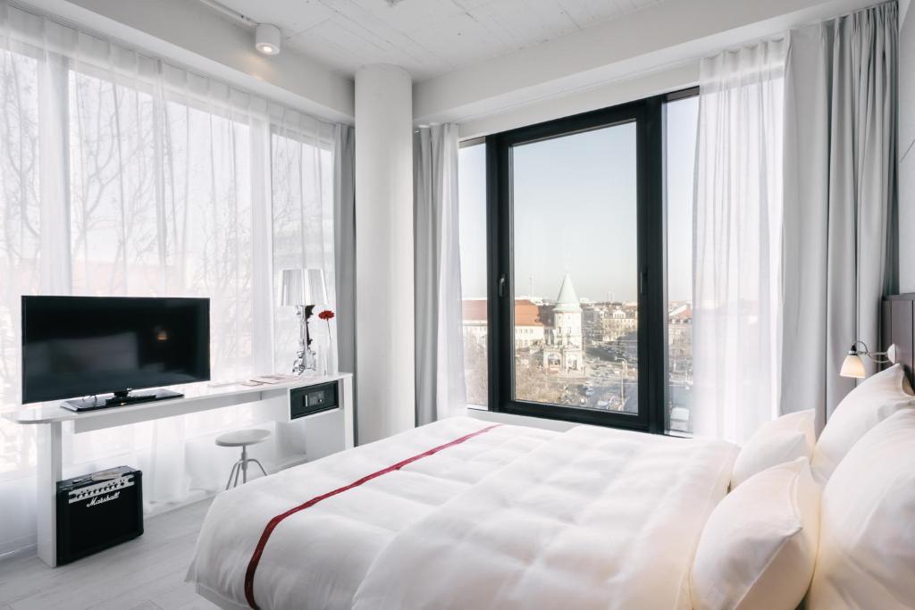 a white bedroom with a large bed and a large window at Ruby Lilly Hotel Munich in Munich