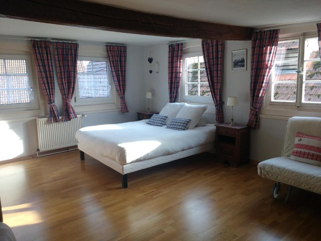 a bedroom with a bed and a chair and windows at Chambres d'hôtes Sabine Billmann in Hunspach