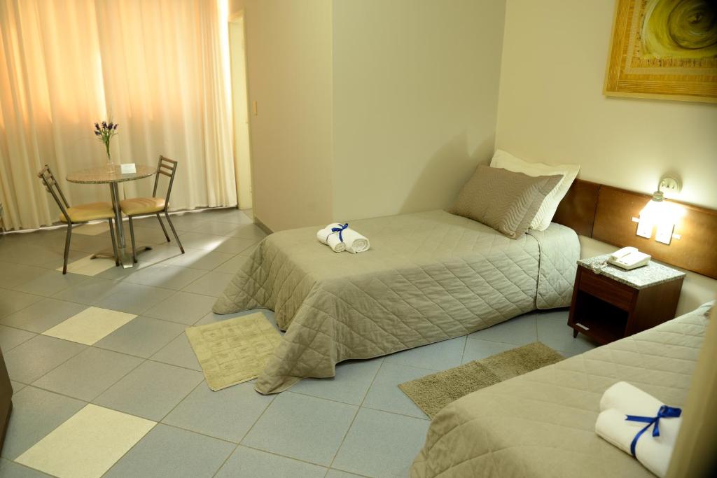 a hotel room with two beds and a table with a chair at Hotel Calypso in Nova Serrana