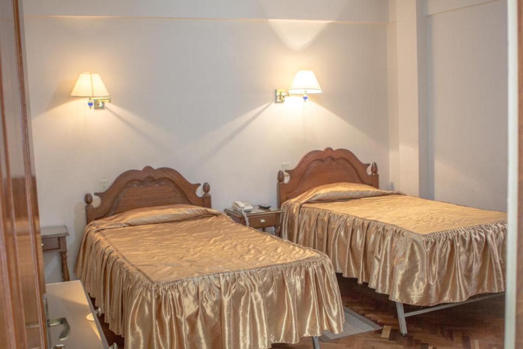 2 camas en una habitación con 2 lámparas en la pared en Hostal España en Sucre