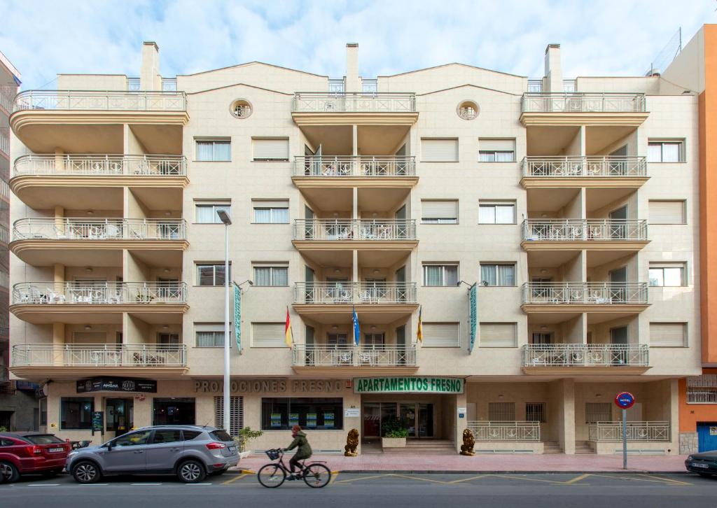 un hombre montando una bicicleta delante de un edificio en Apartamentos Turísticos Fresno, en Torrevieja