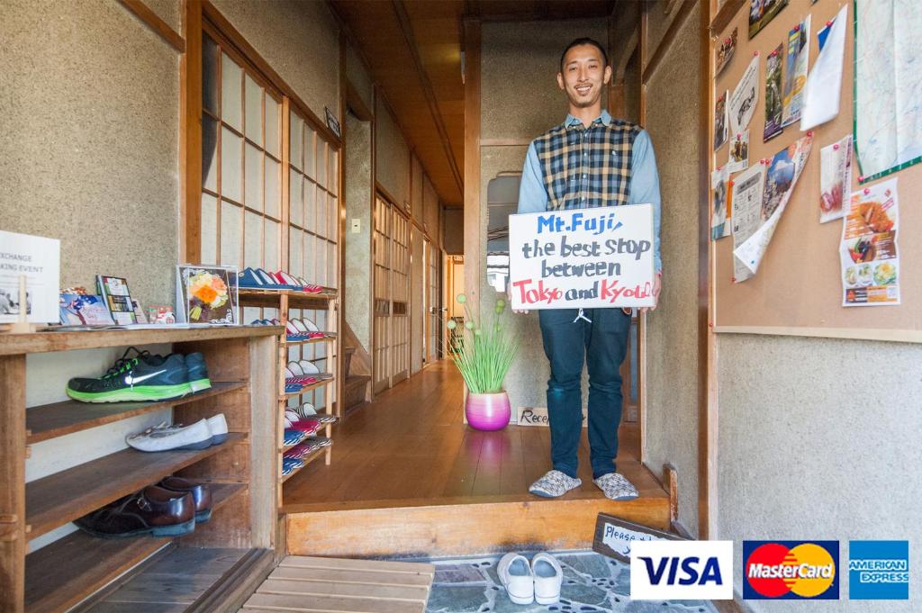 Ein Mann steht im Flur und hält ein Schild. in der Unterkunft NASUBI Mt. Fuji Backpackers in Fuji