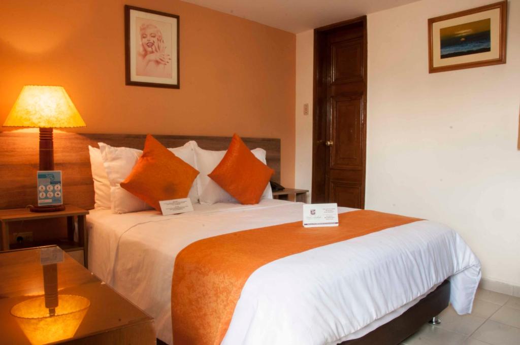 Hotel Ambala Bogota Colonial في بوغوتا: غرفة في الفندق مع سرير كبير مع وسائد برتقالية