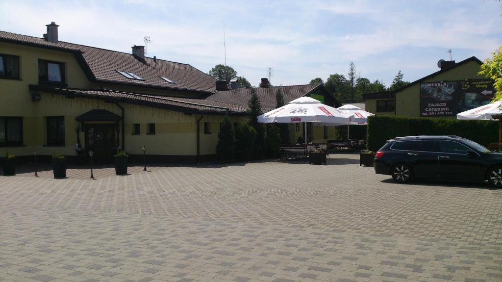 une voiture garée devant un immeuble avec parasols dans l'établissement Zajazd Sielankowe Klimaty, à Kokotek