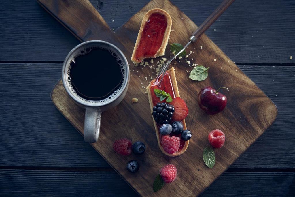 Coffee and berry-topped pastries arranged on a wooden serving board.