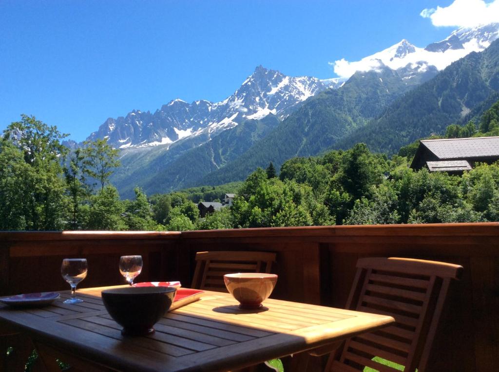 a wooden table with two wine glasses on a balcony with mountains at Facing the Chamonix Needles in Les Houches