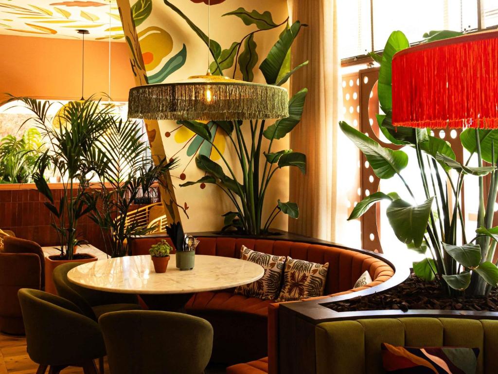 A plant-filled lounge has a round table, curved banquette and upholstered chairs.