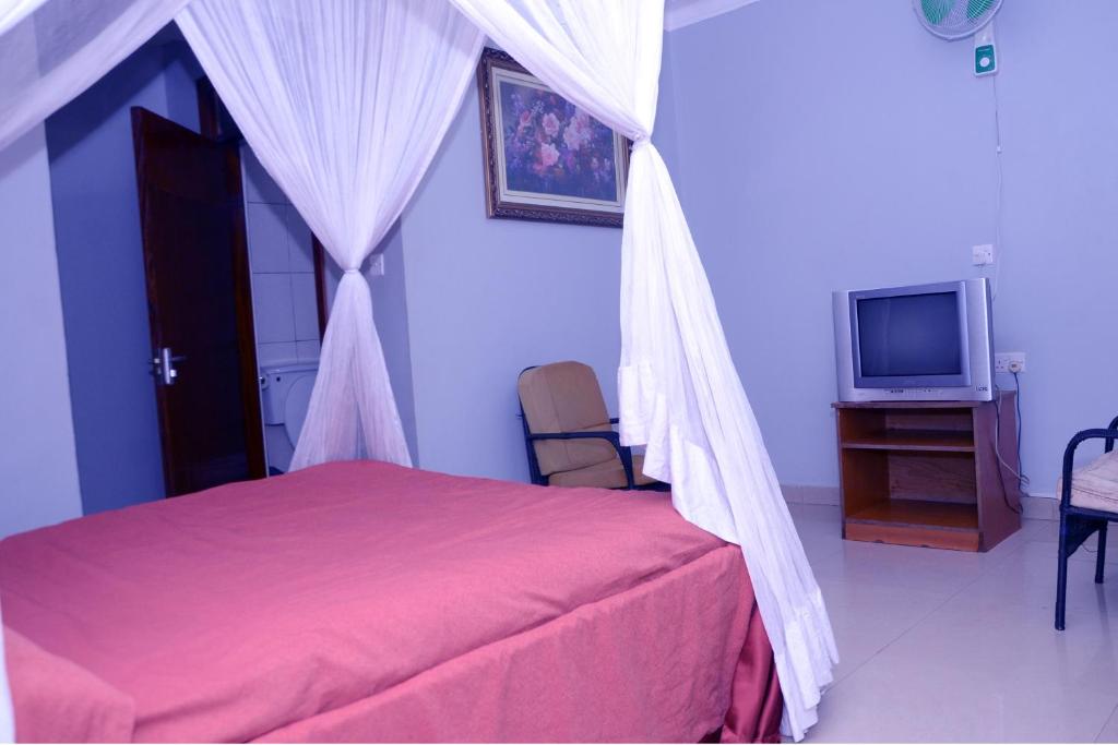 ein Schlafzimmer mit einem Himmelbett und einem TV in der Unterkunft Jaguar Hotel Kampala in Kampala