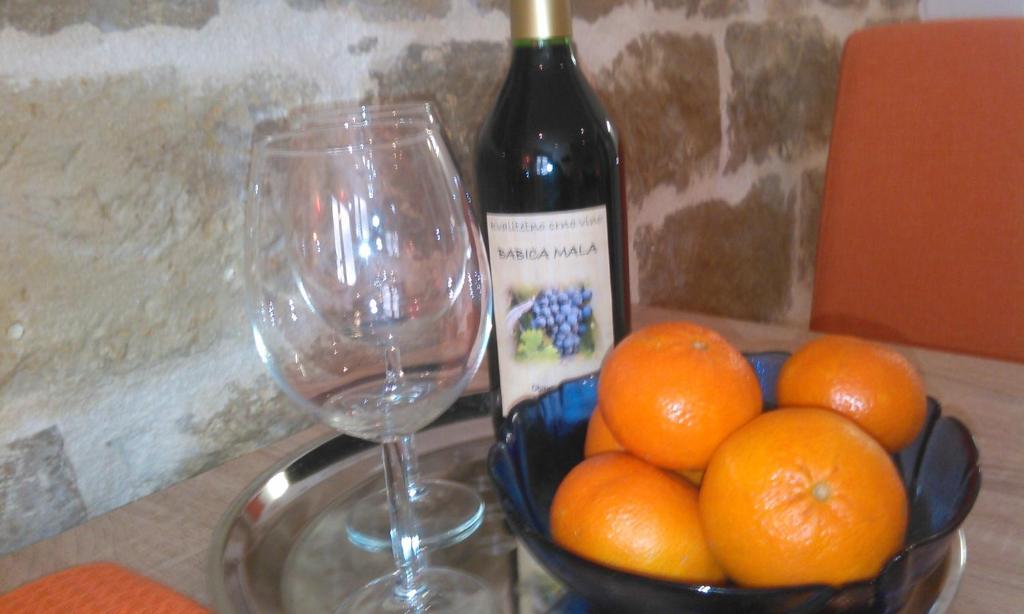 een fles wijn en een kom sinaasappels en een glas bij Apartman Dražin in Kaštela