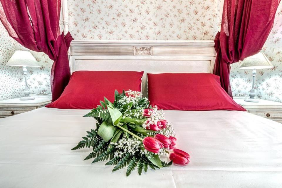 ein weißes Bett mit roten Kissen und einem Blumenstrauß in der Unterkunft Bebeto Suite in Korfu-Stadt