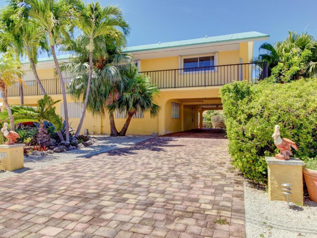 a yellow house with palm trees and a driveway at Canal-side Charisma in Key Colony Beach