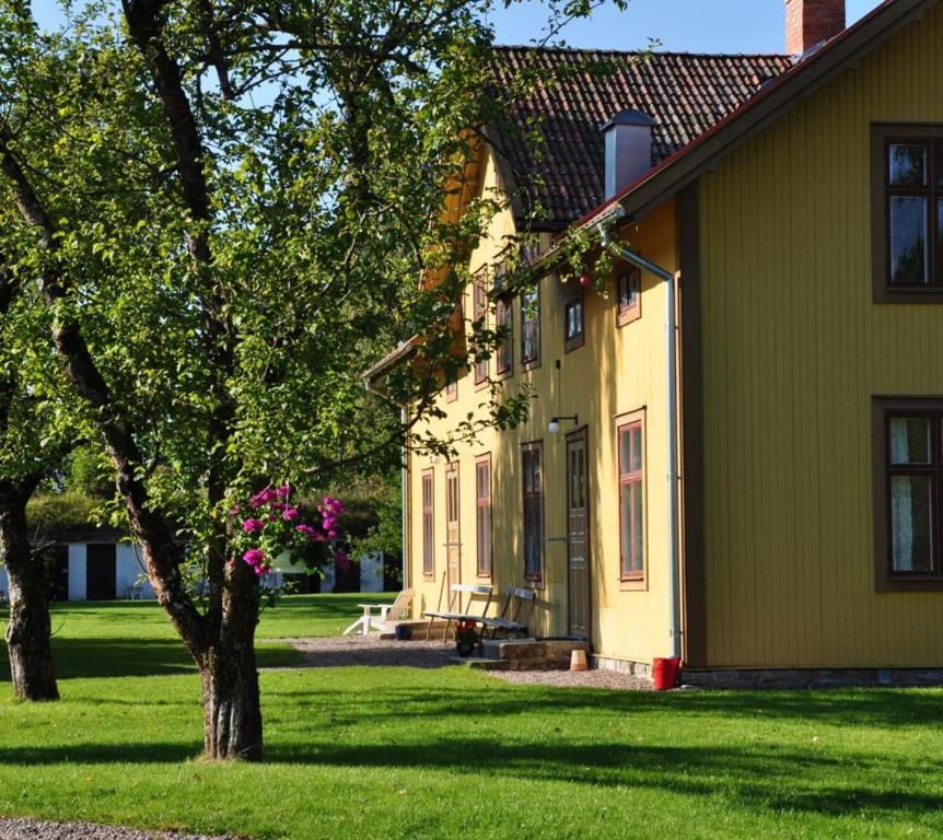 una casa amarilla con un árbol en el patio en STF Glasbruket Hostel & Apartments en Borensberg