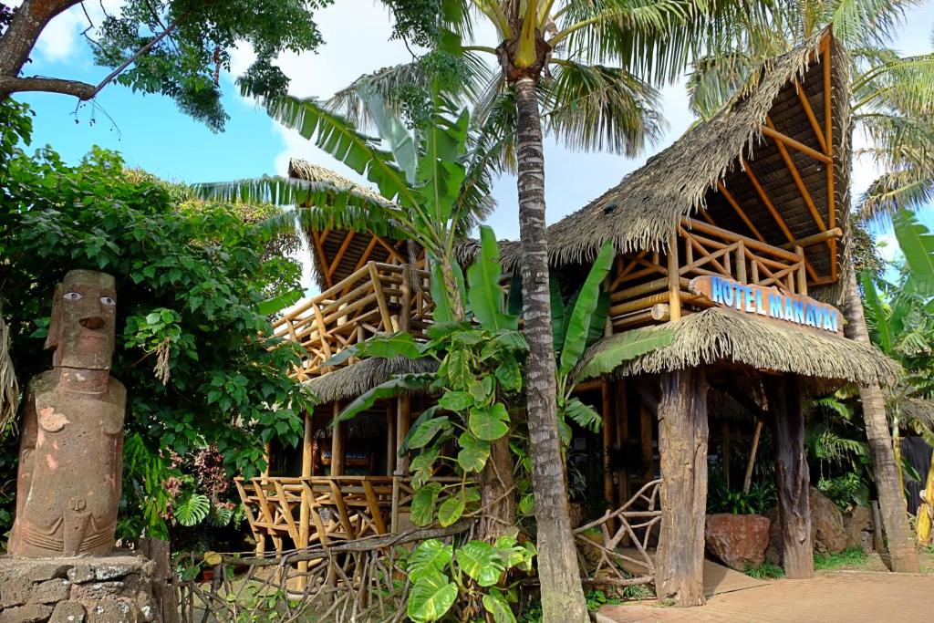 atropical house with a straw roof and a palm tree at Hotel Manavai in Hanga Roa