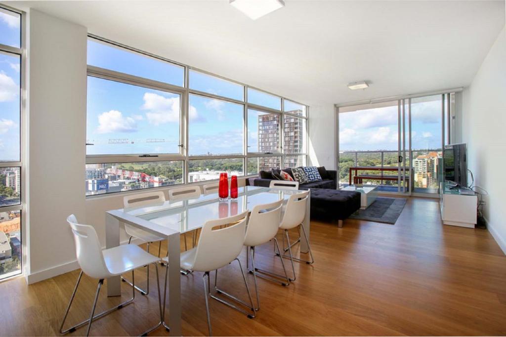 a dining room with a table and chairs and windows at Moore to See - Modern and Spacious 3BR Zetland Apartment with Views over Moore Park in Sydney