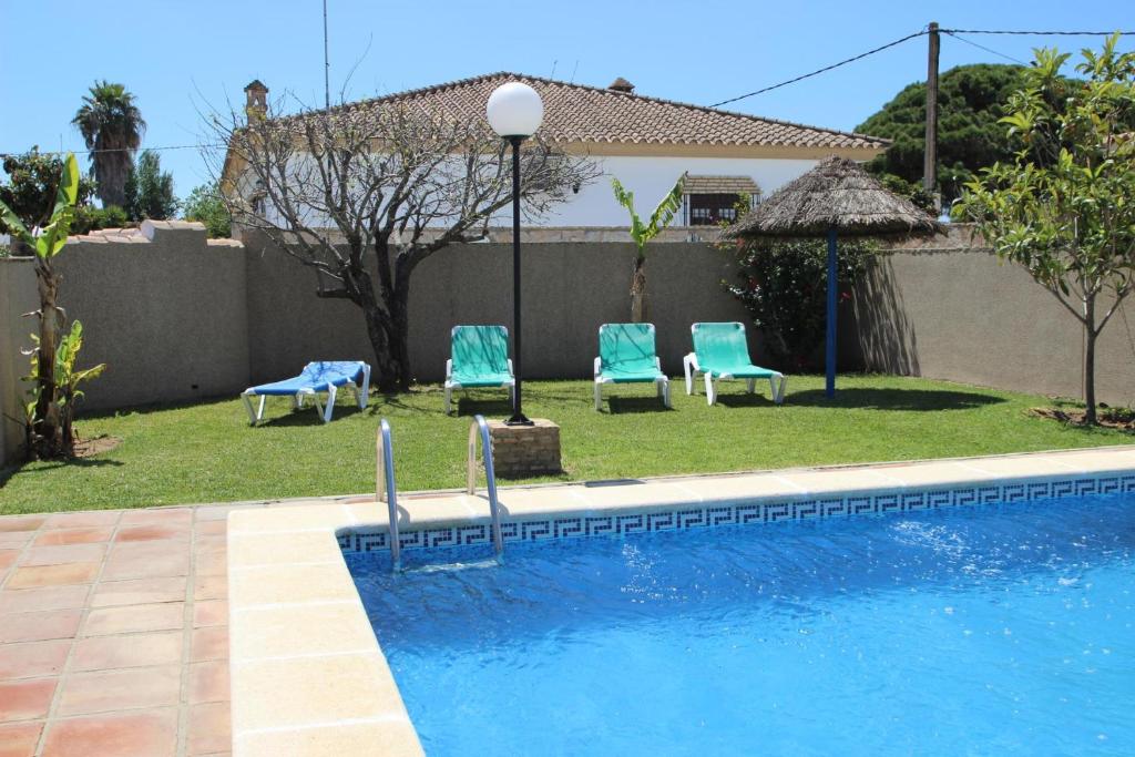 a swimming pool with two blue chairs and a house at Casas Marin in Conil de la Frontera