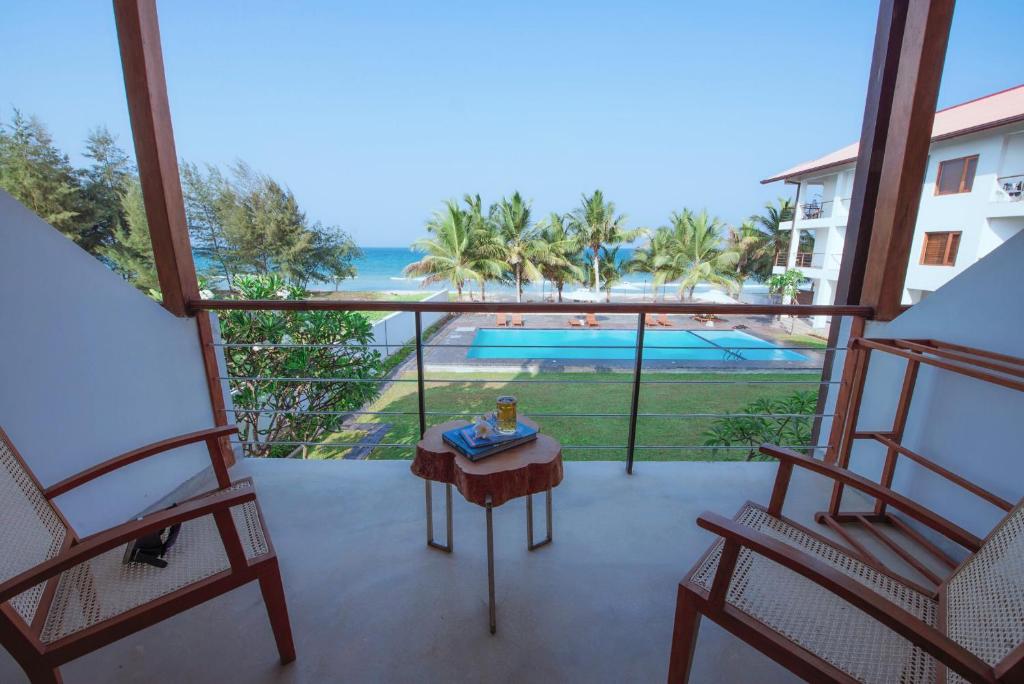 a balcony with two chairs and a table and a view of a pool at Cardamon Hotel Nilaveli in Nilaveli